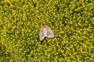 A woman sneezes into a tissue in the middle of a field of flowers.