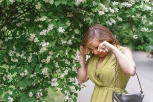 A woman walks under a flowering tree and has watering eyes from hay fever.