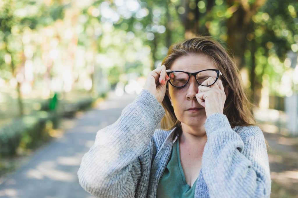 A woman rubs her irritated eye while on a walk.