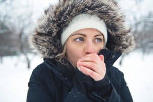 A woman blows on her hands for warmth while outside in winter.