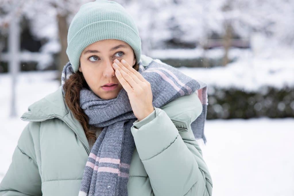 A woman experiences irritated eyes while outside in winter.